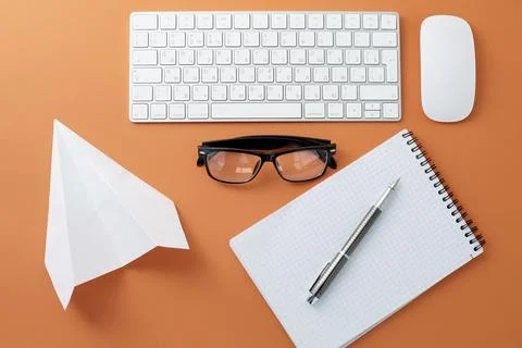 Glasses white keyboard mouse notepad and paper plane on orange background Foto stock