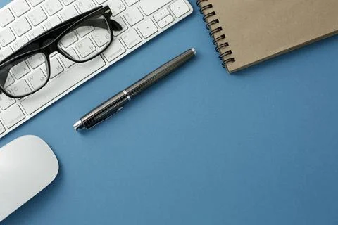 Glasses white keyboard notepad mouse and pen on blue background Stock Photos