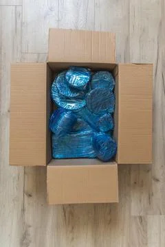 Glassware wrapped with blue wrapping nylon at the bottom of a cardboard box Stock Photos