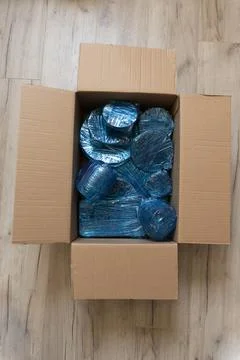 Glassware wrapped with blue wrapping nylon at the bottom of a cardboard box Stock Photos