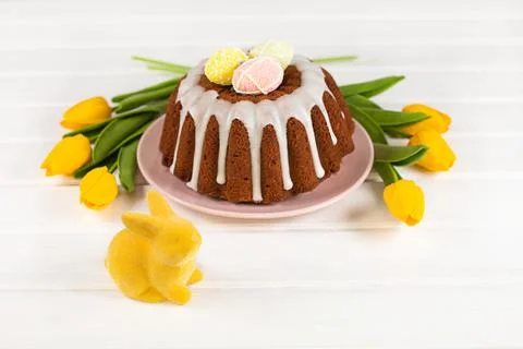 Glazed easter cake decorated with mini eggs, yellow tulips and Easter Bunny Stock Photos