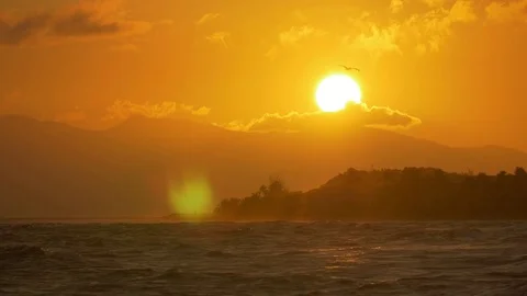 Gleaming sun setting behind the mountain, making the waves of the sea shine Stock Footage 77559640