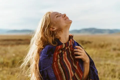 Gleefully throwing her head up a laughing girl in an ethno cape with red hair in Stock Photos