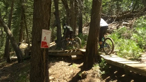 Glide cam shot of two guys mountain biking on a long narrow wooden ramp. Video stock 77578843