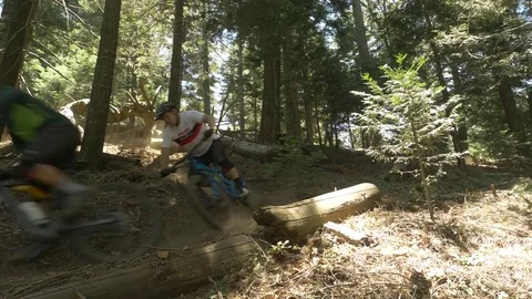 Glide cam shot of two guys on mountain bikes taking a S turn in the woods. Video stock 77584943