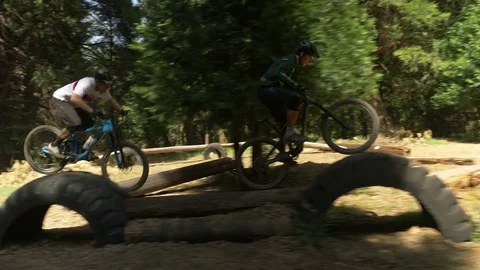 Glide cam shot of two guys mountain biking on a narrow log. Video stock 77586544