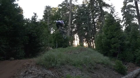 Glide cam shot of two guys mountain biking off a jump at sunset. 動画素材 77852881