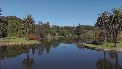 Glide Over Lake While Old Elderly Couple Sit At Park Bench In Park Gardens Stock Footage 274606137