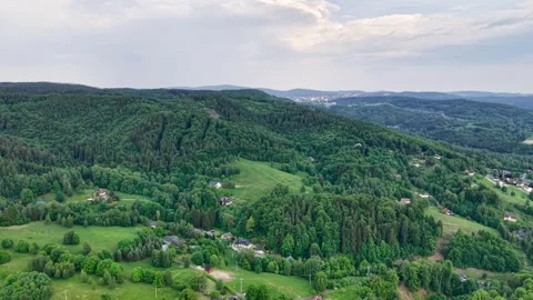 Gliding aerial panorama over dense mixed forest, rolling hills, scattered rural Stock Footage 342359314