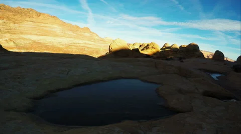 Gliding view over a frozen pool of water as the sun lights up the cliffs. Stockbeeldmateriaal 54054171