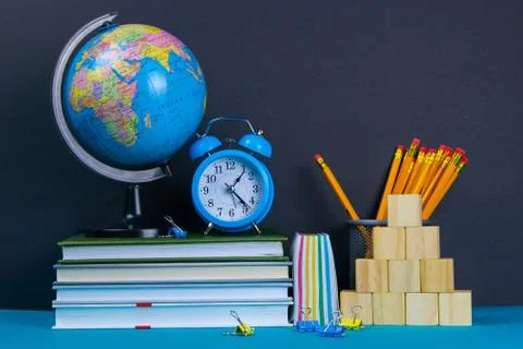 The globe and the clock stand on a stack of books, next to a glass of pencils Stock Photos