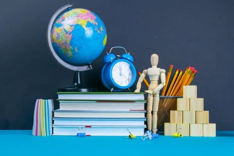 The globe and the clock stand on a stack of books, next to a glass of pencils Stock Photos