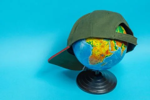 Globe with a green baseball cap on it on a blue background Stock Photos