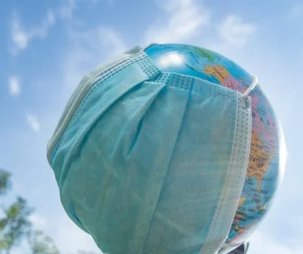 A globe in a medical mask against a blue sky. A worldwide pandemic, the conce Stock Photos