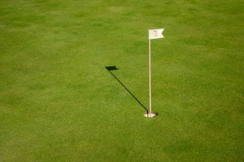 Glof flag mark in hole throwing shadow on the green course grass Stock Photos