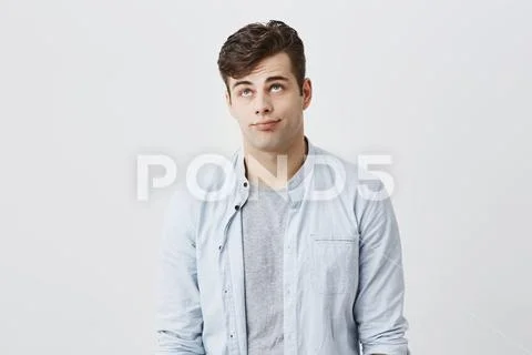 Gloomy caucasian male student frowns face, looking upwards, pouting lips, being Stock Photos