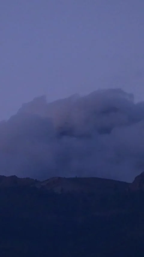 Gloomy clouds moving over a mountain ridge at dusk as the landscape transitions Stock Footage 344786332