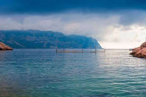 Gloomy dramatic rain clouds over the calm sea and mountains, picturesque land Stock Photos