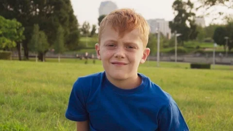 Gloomy face of sad red-haired little boy with freckles, sunny summer day in park Stock Footage 95049344