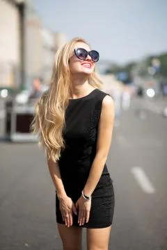 Glorious smiling model wearing black dress and sunglasses, walking down the s Stock Photos