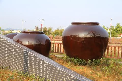 Glossy ceramic jars displayed beside brick wall and wooden fence Stock Photos