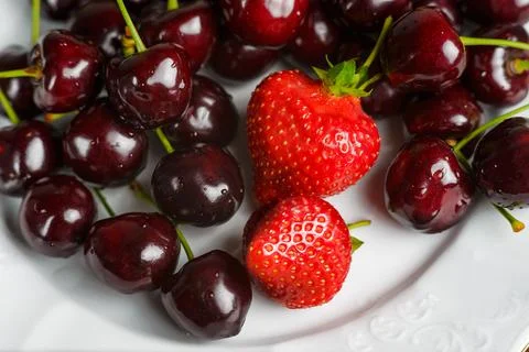 Glossy cherries on a white plate with red strawberries. Stock Photos