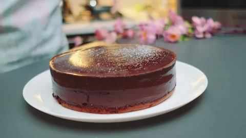 Glossy chocolate mousse cake dusted with powdered sugar on kitchen counter Vidéo 342885606