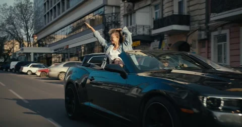 A glossy gray convertible is driving down the street, a blonde girl in the back Video stock 246110945