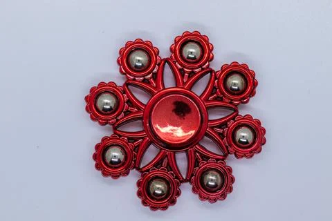 Glossy Red Gear-Shaped Fidget Spinner for Stress Relief on Plain Surface Stock Photos
