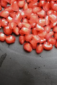 Glossy Ruby Pomegranate Seeds on Black Stone Background 库存照片