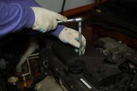 A gloved auto mechanic concentrates on using a ratchet wrench to replace spark Fotos de archivo