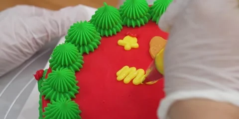 Gloved Baker Decorating Red Cake with Green and Yellow Frosting Stock Footage 343588551