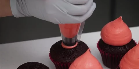 Gloved Baker Piping Bright Orange Frosting on Chocolate Cupcakes Stock-Footage 343588787