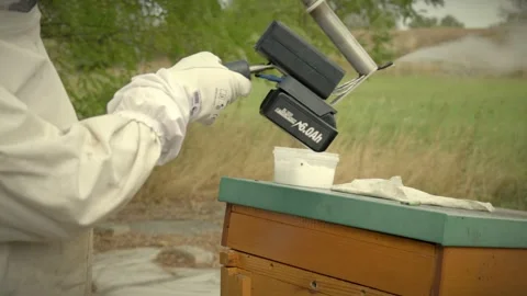 Gloved beekeeper using a battery powered heated tool beside wooden hives 스톡 동영상 347847101