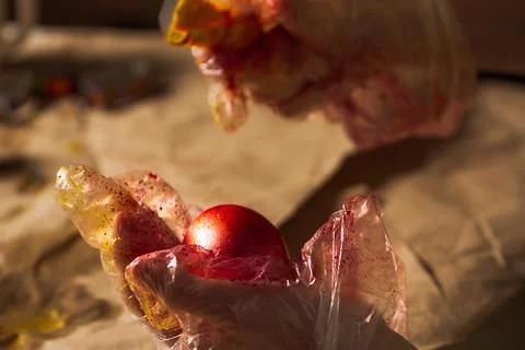 Gloved boy's hands paint Easter egg red Stock Photos