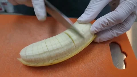 Gloved Chef Hands Slicing a Fresh Banana on an Orange Cutting Board Stock Footage 345652096