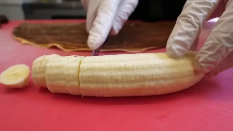 Gloved Chef Hands Slicing Fresh Banana on Red Cutting Board Stock Footage 345692132