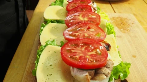 A gloved chef prepares a sandwich with meat, tomato and cheese on lettuce leaves Stock Footage 134903230