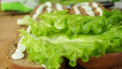 A gloved chef puts lettuce leaves on a large sandwich. 4K Stock Footage 134903129