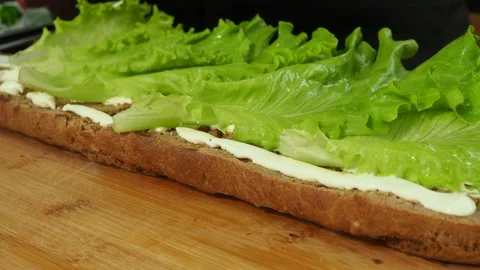 A gloved chef puts lettuce leaves on a large sandwich. 4K Stock Footage 134903269