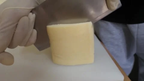 Gloved Chef Slicing Block of Cheese with Cleaver on Cutting Board Vídeo Stock 343587522