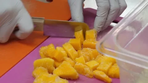 Gloved Chef Slicing Frozen Mango Cubes on Pink Cutting Board Stock Footage 345692254
