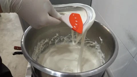 Gloved chef stirring thick white liquid or batter in a large stainless steel pot Stock Footage 345291818