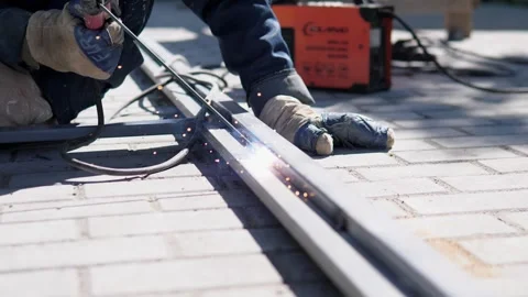 Gloved construction worker grinding metal rail beside brick paving, sparks Stock-Footage 344873218