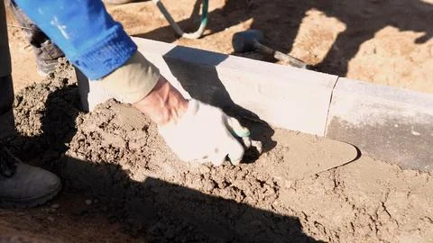 Gloved construction worker spreading wet mortar around concrete blocks in Stock Photos
