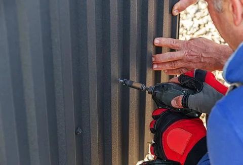 A gloved construction worker uses a drill driver to drive a screw into a dark Foto stock