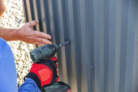 A gloved construction worker uses a drill driver to drive a screw into a dark Foto stock
