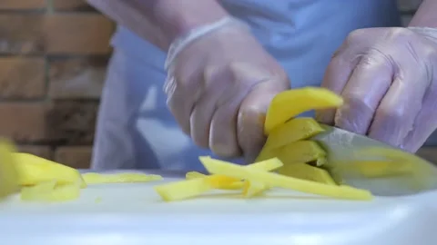 Gloved cook cuts a ripe mango into small pieces with a large knife. Stock Footage 131996583