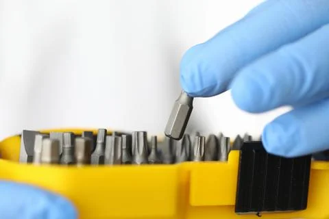 Gloved craftsman pulls out screwdriver and screwdriver heads from yellow box Stock Photos