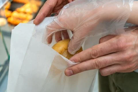 Gloved customer placing fresh bread roll into paper bakery bag in grocery sto Stock-Fotos